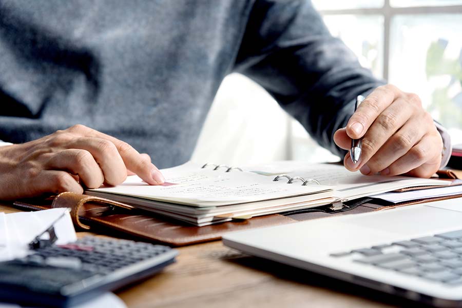 Person with a grey sweatshirt holding a grey pen and a white pad of paper ready to write information down