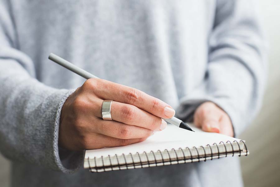 Person with a grey sweatshirt holding a grey pen and a white pad of paper ready to write information down