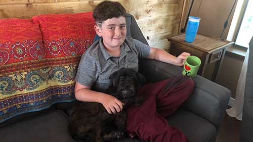 boy on couch with drink cuddling with black dog on his lap