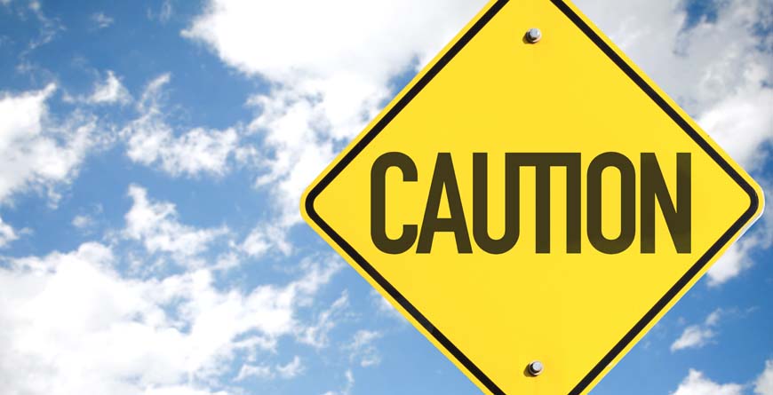 a yellow sign that says caution in black lettering with a blue shy and white clouds in the background